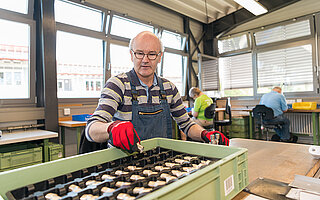 Beschäftigter der WfbM am Arbeitsplatz beim Einsortieren von Drehteilen in eine Kunststoff-Box