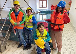 drei Kinder/Jugendliche mit Sinnesbehinderung und Lehrerin mit Bauhelmen im "Bädle" Baindt