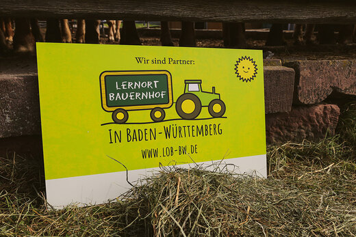 Schild "Partner Lernort Bauernhof" im Heu stehend