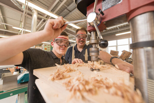 Schreinermeister und Azubi arbeiten an einer Ständerbohrmaschine in der Werkstatt