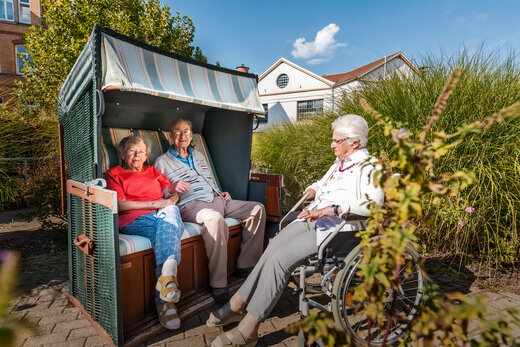 ältere Menschen im Garten - eine Dame im Rollstuhl, die anderen in einem Strandkorb sitzend