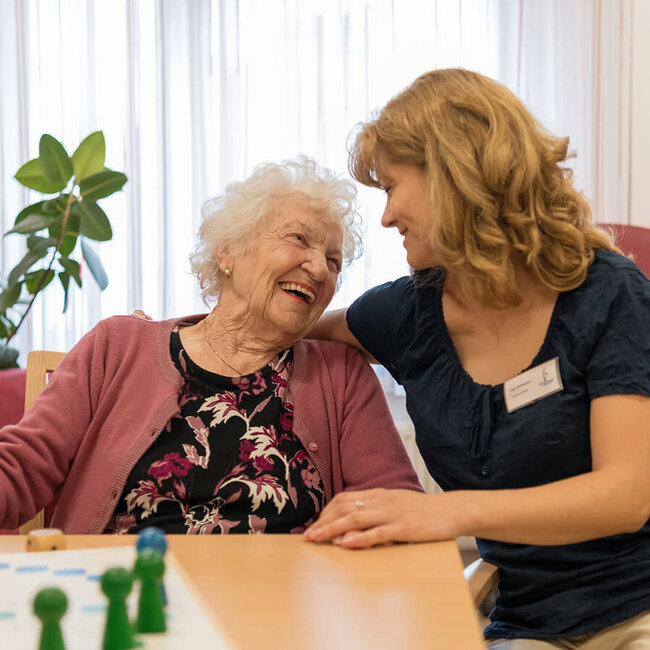 Betreuerin und Seniorin spielen gemeinsam ein Brettspiel