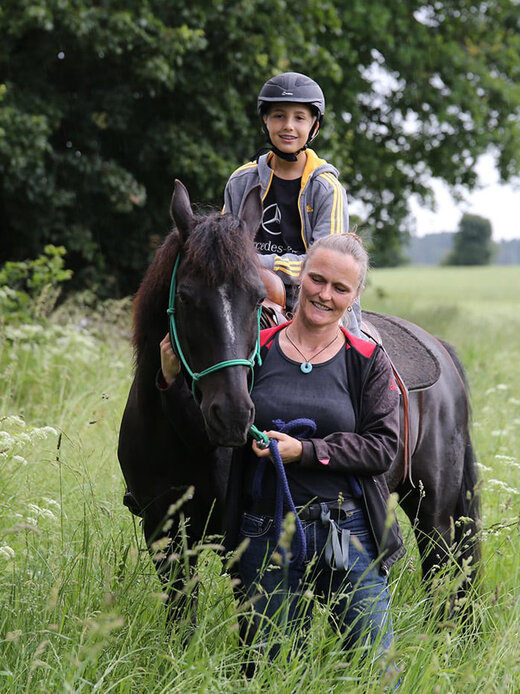 Reittherapeutin mit Pferd an der Leine, auf dem eine Klientin sitzt