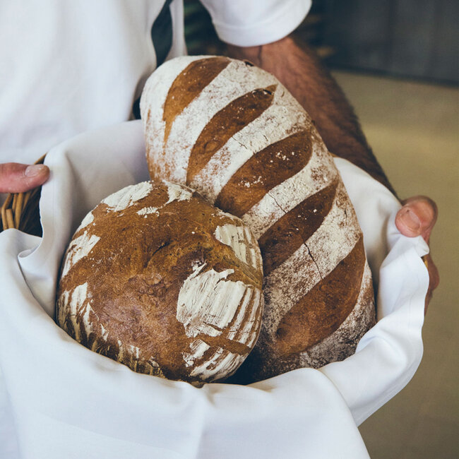 Bäcker hält Brotkorb mit zwei Broten in der Hand