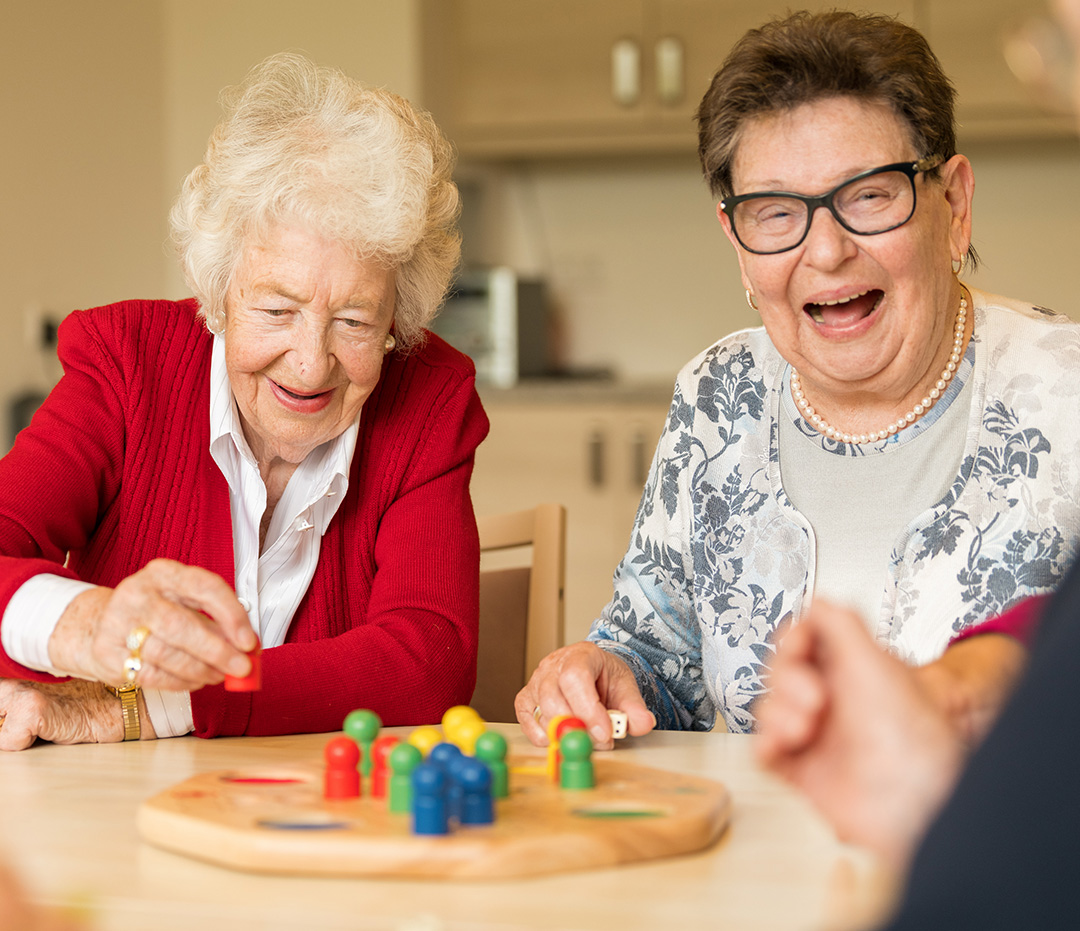 zwei ältere Damen lachen beim Spielen eines Brettspiels