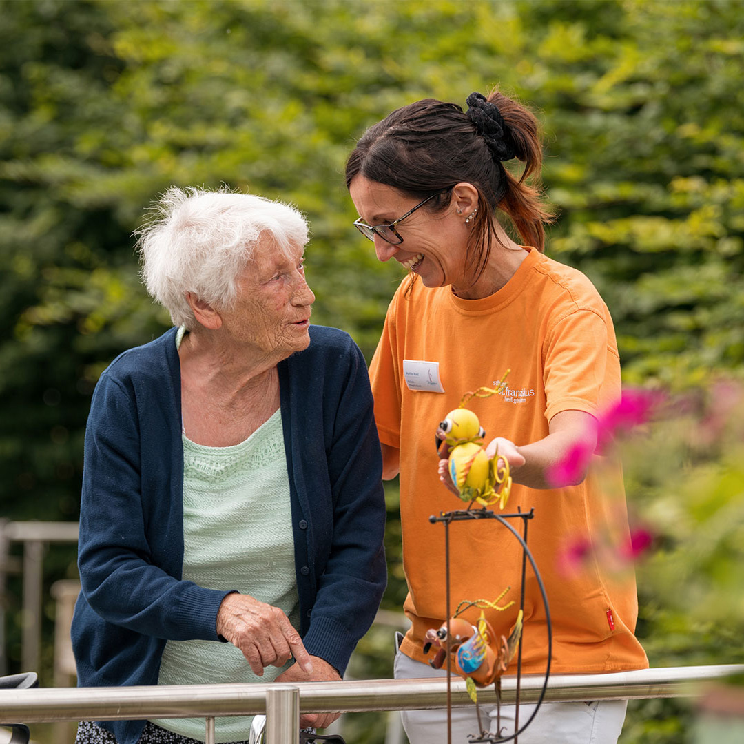 ältere Dame mit Gehstock unterhält sich mit Betreuerin im Garten