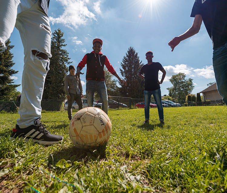 Vier Jugendliche spielen Fußball auf Freigelände