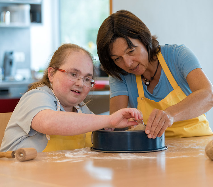 Frau mit Sehbehinderung und Betreuerin backen einen Kuchen