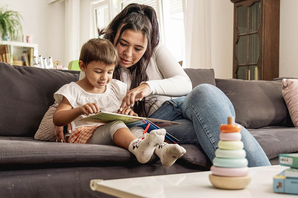 Junge Mitarbeitende sitzt mit einem Jungen auf einer Couch, die beiden lesen ein Buch