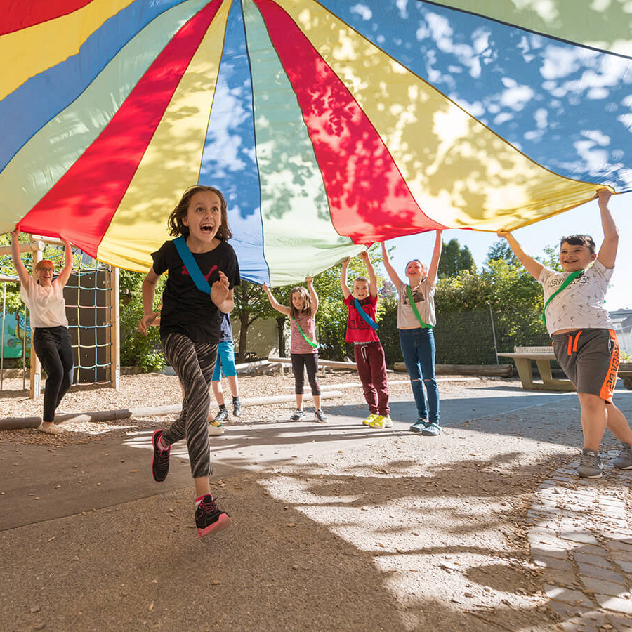 Kinder spielen unter einem bunten Fallschirm-Schwungtuch